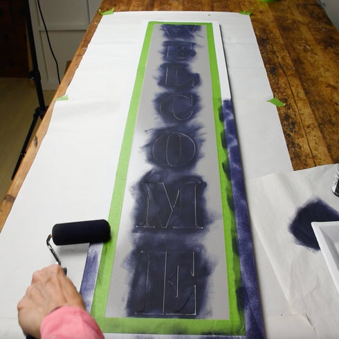 Large custom magnetic stencil displaying the word 'WELCOME' being painted on a wooden surface.